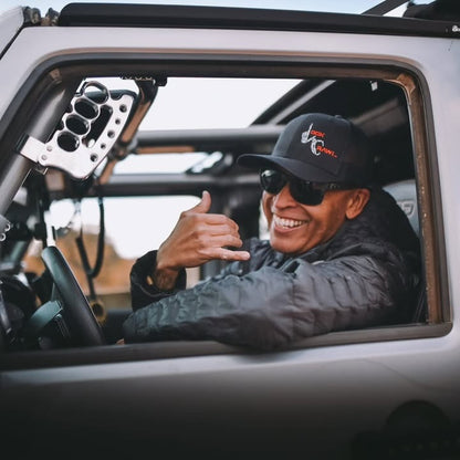 Person sitting inside a vehicle, wearing a cap and sunglasses, with a blurred background.