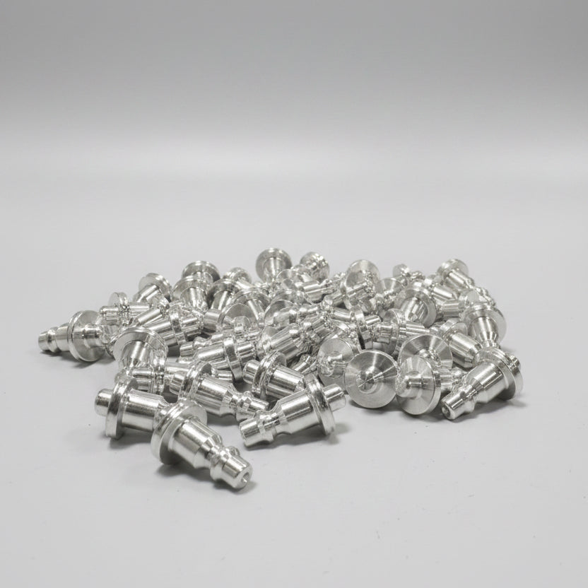 A pile of machined silver aluminum coupler corks with resting on a blue workbench in an industrial workshop setting with a CNC machine in the background.