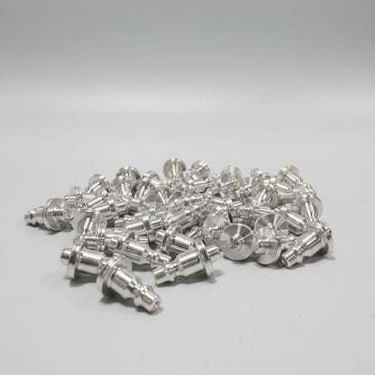 A pile of machined silver aluminum coupler corks with resting on a blue workbench in an industrial workshop setting with a CNC machine in the background.